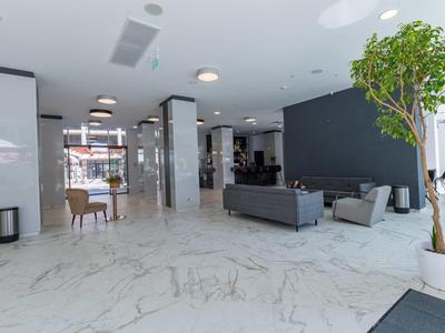 Moderna recepción de hotel con suelo de mármol, sofás grises, sillas y un gran árbol en maceta.