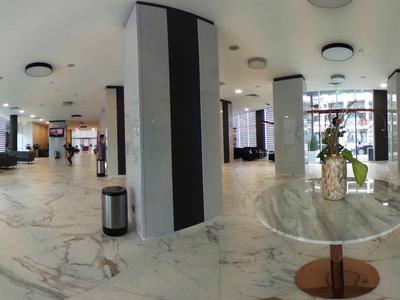 Moderna recepción de hotel con asientos, suelo de mármol y gran entrada con mucha luz natural.