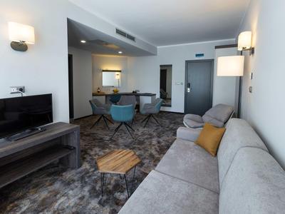 Modern hotelkamer met bank, tv en eettafel in neutrale tinten.