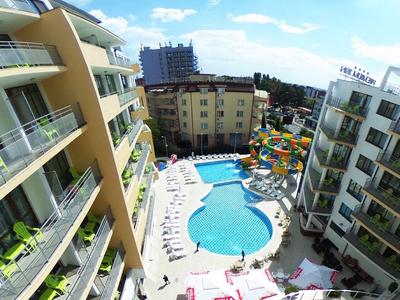 Uitzicht op een hotel met een groot buitenzwembad en glijbanen onder een blauwe hemel.