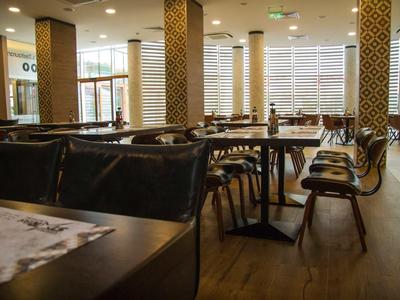 Interior moderno de restaurante con suelo de madera, sillas negras y columnas con patrones geométricos.