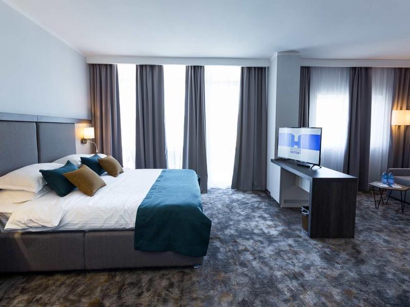 Moderne hotelkamer met groot bed, tv en zithoek in neutrale kleuren.