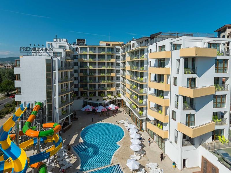 Groot meerlaagss hotel met buitenzwembad en kleurrijke glijbanen bij zonnige lucht.