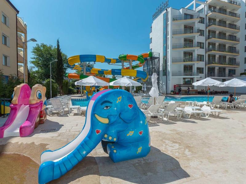 Kleurrijk glijbaangebied voor kinderen met waterspeeltuin naast hotelgebouwen op zandstrand.