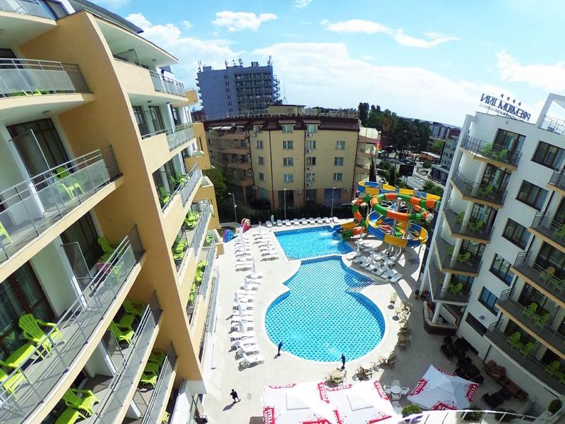 Uitzicht op een hotel met een groot buitenzwembad en glijbanen onder een blauwe hemel.