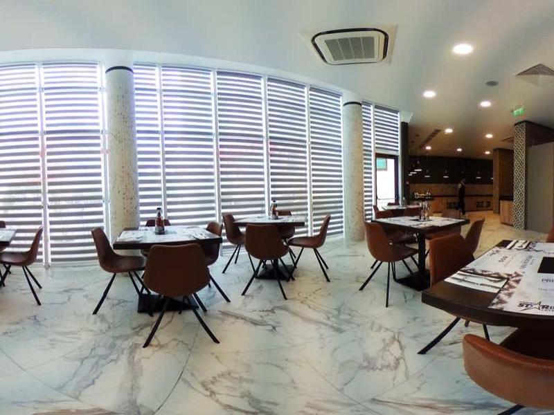 Lichte hotel eetruimte met modern meubilair en grote ramen met jaloezieën.