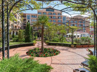 Uitzicht op een verzorgde tuin met palmbomen en bloemen voor een meerlaagse hotelgebou.