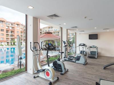 Fitnessruimte met cardioapparatuur en uitzicht op het zwembad en aangrenzende gebouwen.