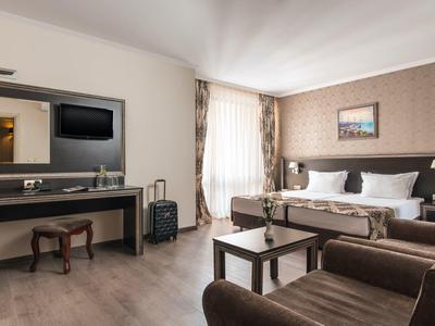 Ruime hotelkamer met tweepersoonsbed, zithoek en bureau met tv.