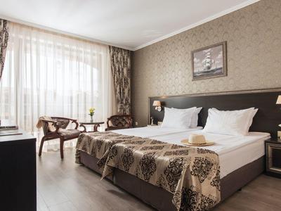 Modern hotelkamer met tweepersoonsbed, fauteuils en grote ramen met gordijnen