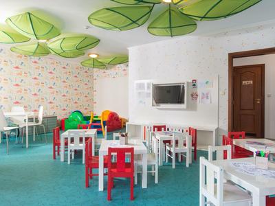 Kinderspeelkamer met kleurrijke stoelen, witte tafels en verfrissende bladvormige plafondlampen