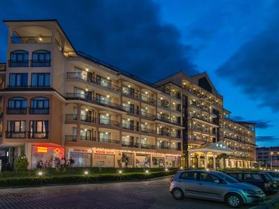 Groot meerlaag hotelgebouw bij schemering met verlichte balkons en geparkeerde auto's.