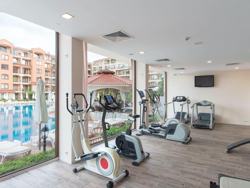 Fitnessruimte met cardioapparatuur en grote ramen met uitzicht op het zwembad en het hotelgebouw.