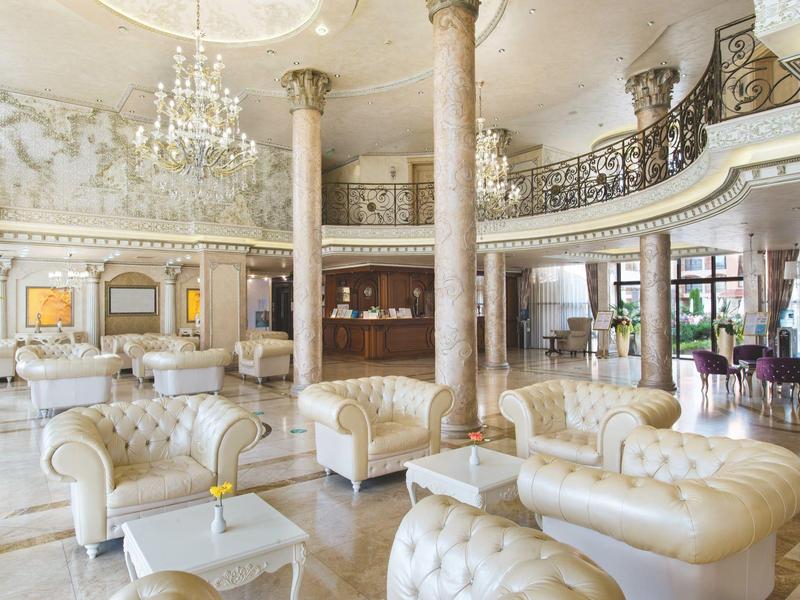 Elegante hotel lobby met kroonluchters, wit meubilair en marmeren zuilen.