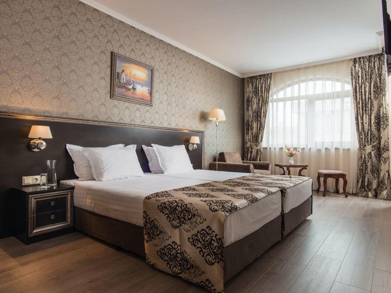 Gezellige hotelkamer met twee bedden, gordijnramen en houten vloer.