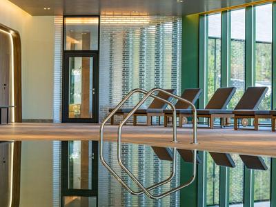 Modet binnenzwembad met ligstoelen en grote ramen in een hotel.