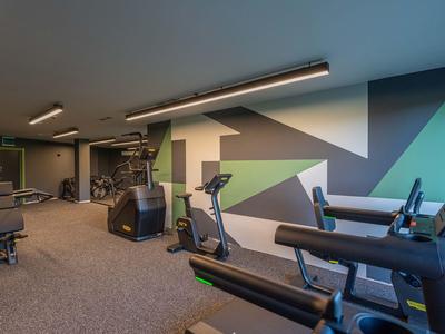 Modernes Hotel-Fitnessstudio mit verschiedenen Trainingsgeräten und farbiger Wandgestaltung.