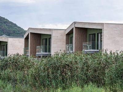 Moderne hotelkamers met balkons achter hoog gras en heuvelachtergrond.