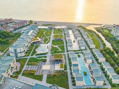 Luftaufnahme eines modernen Hotelresorts am Meer mit Swimmingpools und Grünflächen.