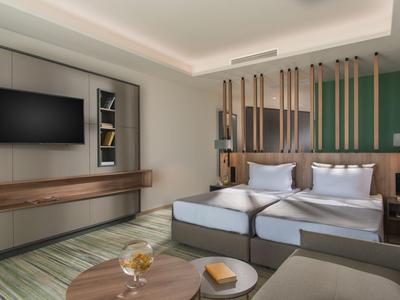 Modern ingerichte hotelkamer met tweepersoonsbed, tv en gezellige zithoek.