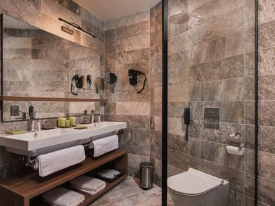 Moderne hotelbadkamer met stenen tegels, dubbele wastafels en inloopdouche.