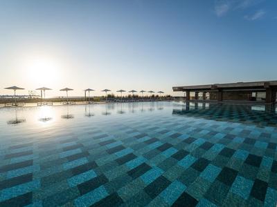 Großer Infinity-Pool bei Sonnenuntergang mit Sonnenschirmen am Rand.