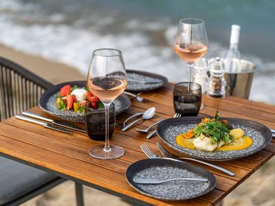 Restaurant-Tisch am Meer mit zwei gedeckten Tellern und Gläsern Roséwein