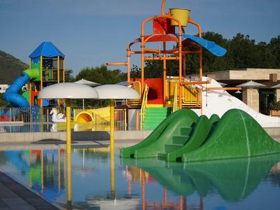 Kleurrijke waterspeelplaats met glijbanen bij een hotelzwembad.