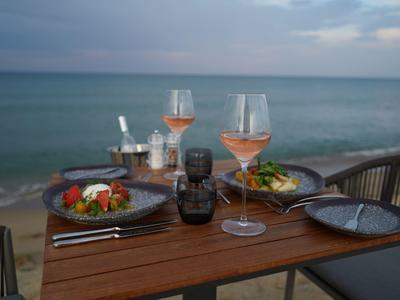 Tafel met eten en wijnglazen bij zee bij zonsondergang.