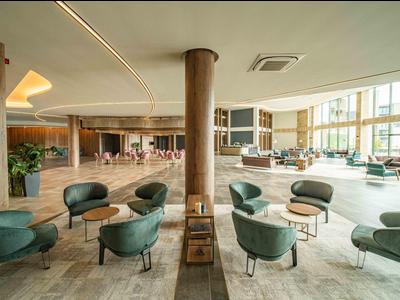 Ruime, lichte hotel lounge met groene fauteuils en uitzicht op het zwembadgedeelte.