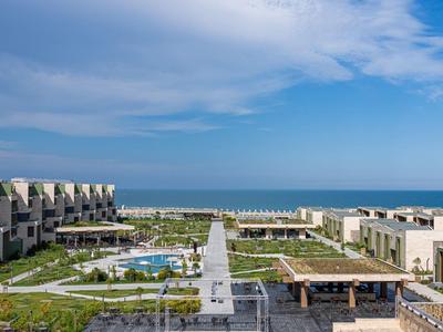 Modern hotelcomplex met zwembad en uitzicht op zee onder een blauwe lucht.