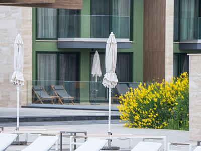 Moderne hotelzwembad met ligstoelen, parasols, gele bloemen en balkons op de achtergrond.