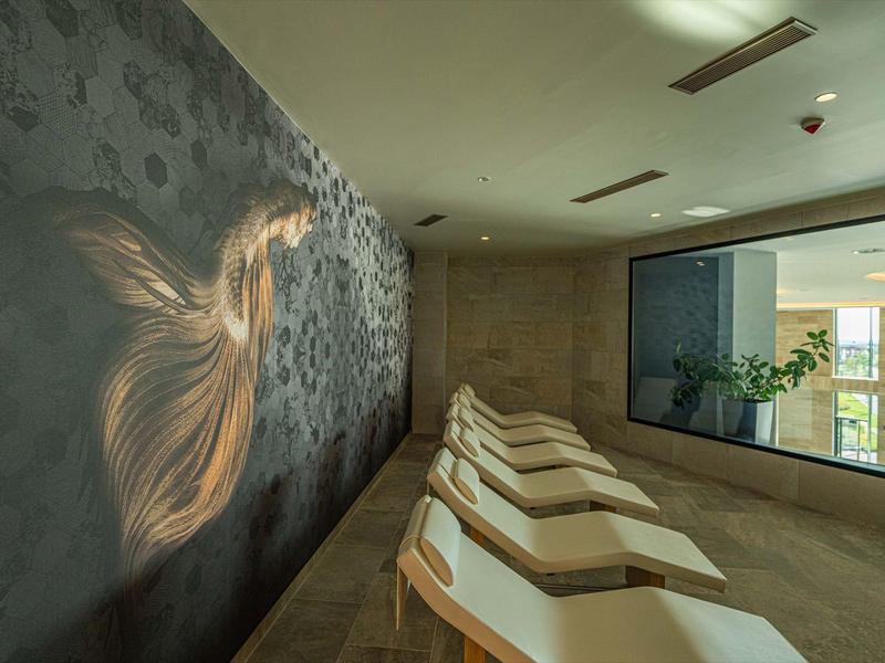 Ontspanningsruimte met comfortabele ligstoelen, groot raam en muur met abstract patroon.