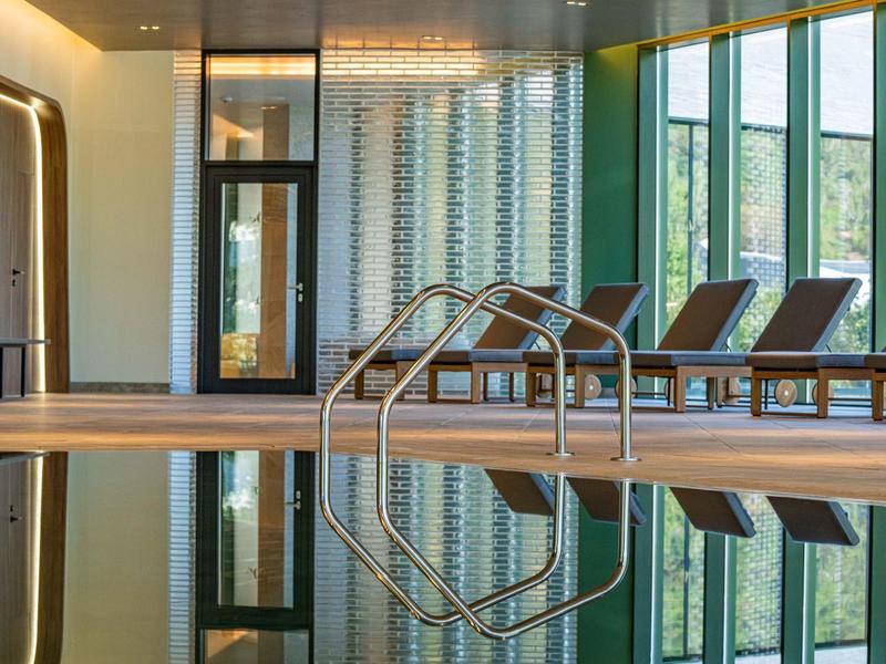 Modet binnenzwembad met ligstoelen en grote ramen in een hotel.