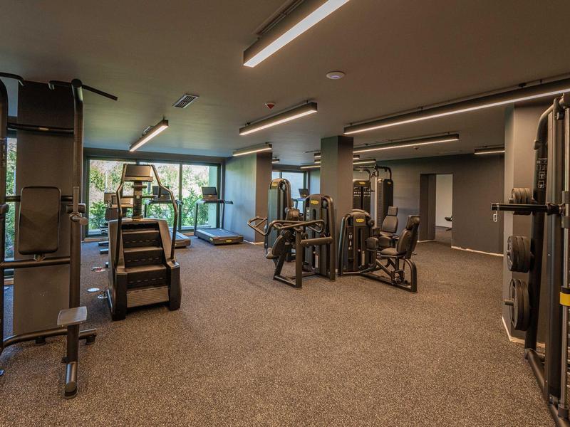 Ruime fitnessruimte met moderne trainingsapparatuur en grote ramen.