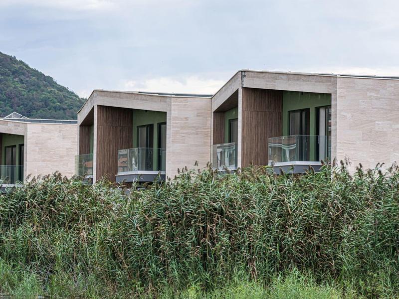 Moderne hotelkamers met balkons achter hoog gras en heuvelachtergrond.