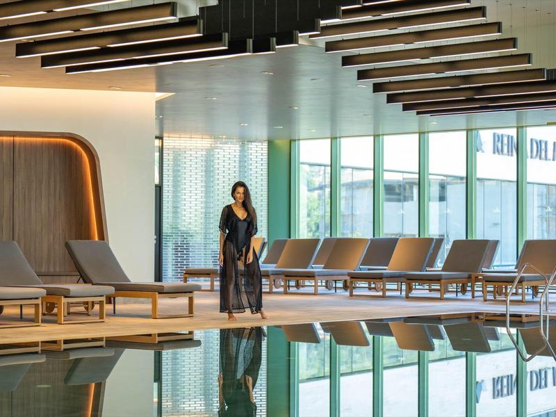 Elegant binnenzwembad met ligstoelen en grote ramen, persoon in badjas.