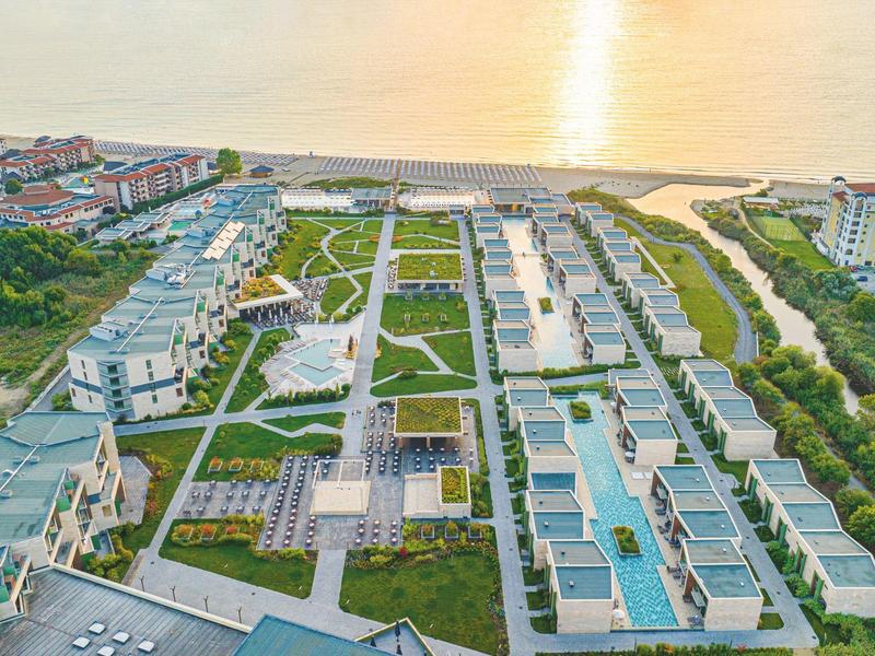 Luchtfoto van een groot hotelcomplex aan zee met meerdere gebouwen bij zonsondergang.