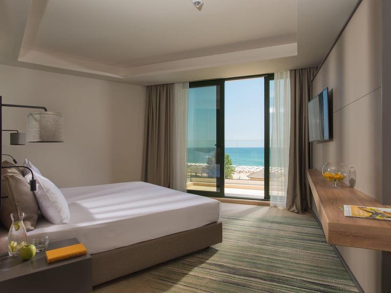 Moderne hotelkamer met tweepersoonsbed en zeezicht via grote ramen.