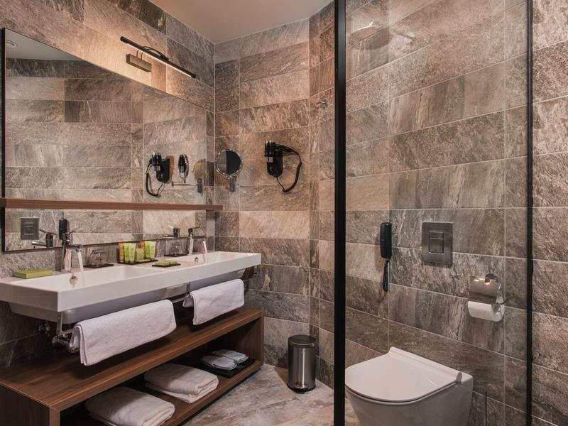 Moderne hotelbadkamer met stenen tegels, dubbele wastafels en inloopdouche.