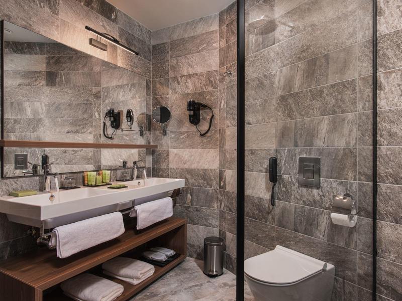 Moderne badkamer met natuurstenen muren, dubbele wastafels en inloopdouche.