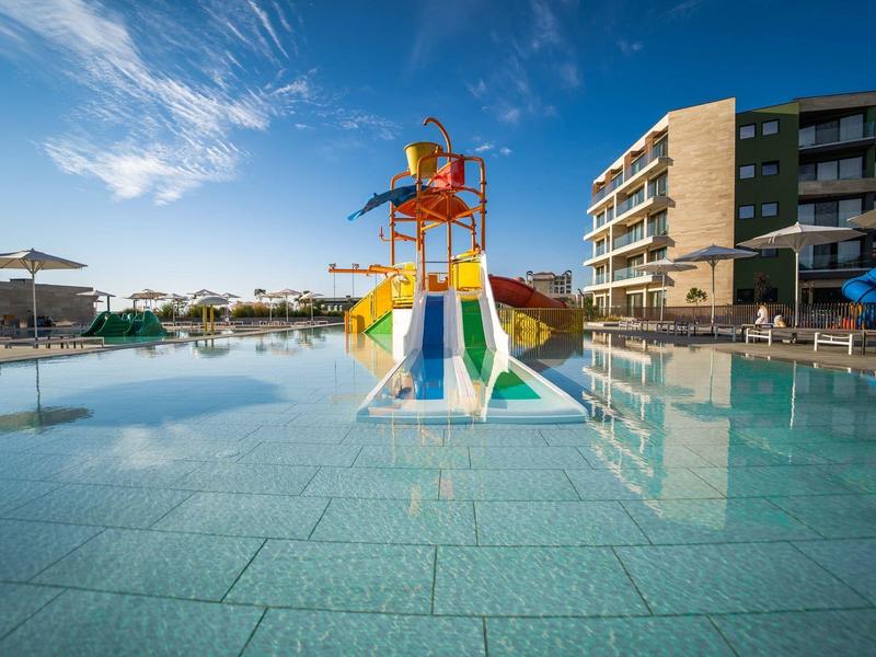 Kinderwaterslides in een groot ondiep zwembad voor een hotel bij helder weer.