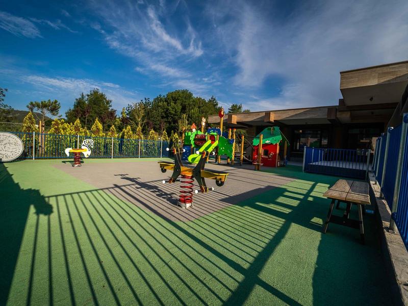 Speeltuin met kleurrijk speeltoestel en schaduwen op groene ondergrond bij zonnige hemel.
