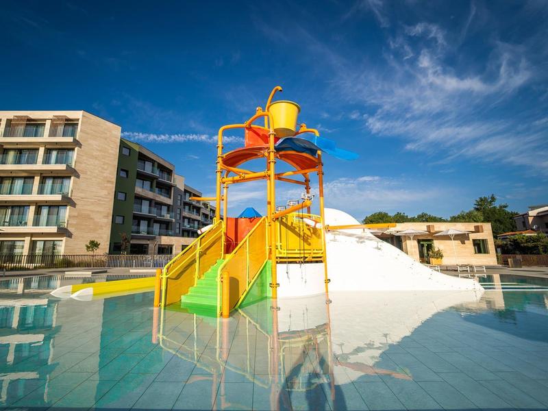 Kleurrijke waterspeeltuin met glijbanen in een hotelzwembad onder een blauwe lucht.
