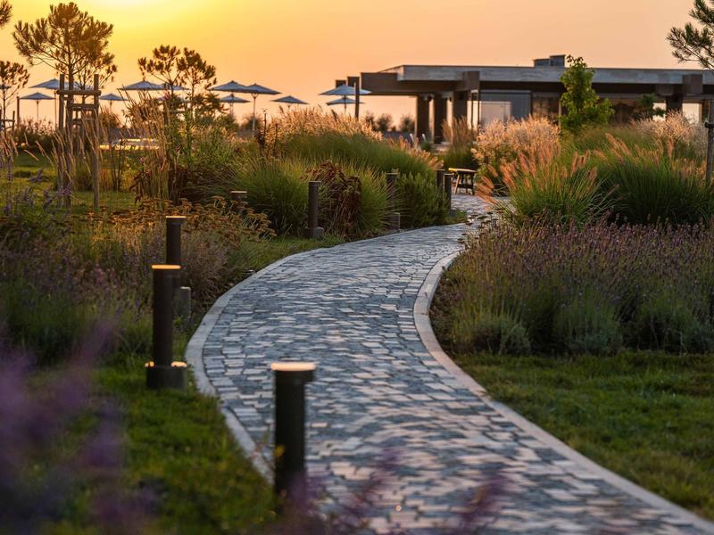 Gebogen geplaveid pad door tuin bij zonsondergang met lichten langs het pad.
