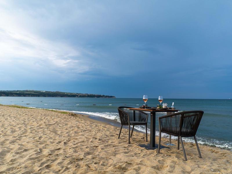 Tafel en stoelen op zandstrand met uitzicht op rustige zee onder bewolkte lucht.