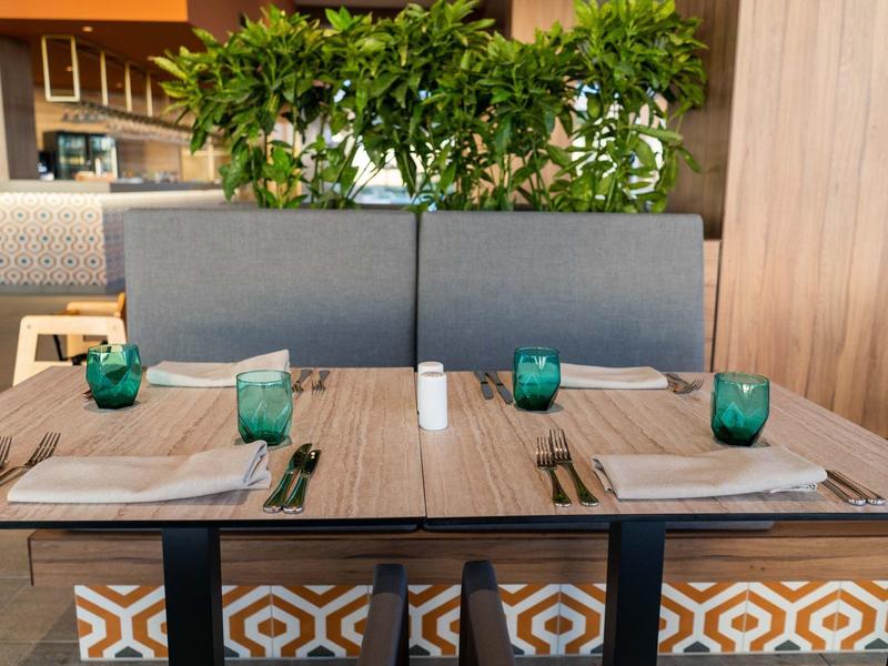 Modern eettafel met blauwgroene glazen en grijze banken in een restaurant.