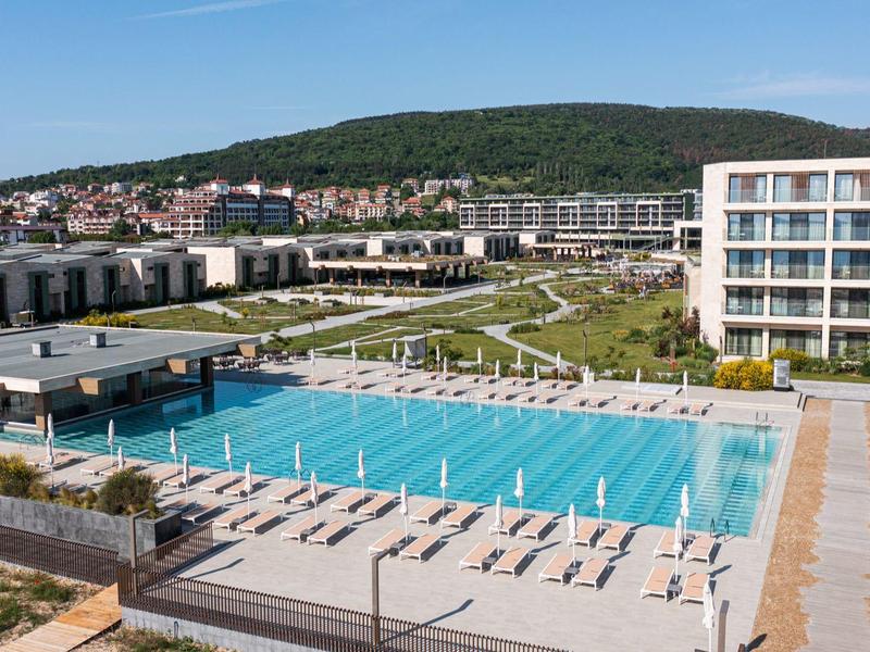 Modern hotelcomplex met groot buitenzwembad en ligstoelen onder een heldere lucht.