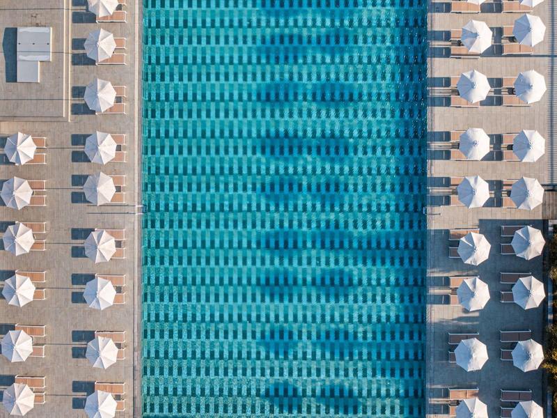 Luchtfoto van een lang zwembad met witte ligbedden en parasols aan beide zijden.