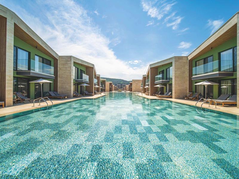 Modern buitenzwembad tussen twee rijen hotelkamers onder een heldere lucht.